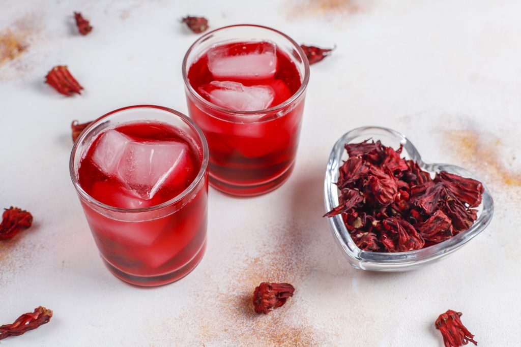 2 cups of hibiscus tea with ice and a heart-shaped bowl filled with hibiscus flowers